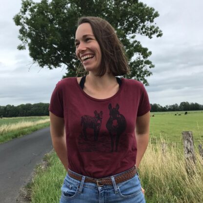 Lachende Frau mit burgundrotem T-Shirt handbedruckt mit einem Linolschnitt der zwei Esel zeigt