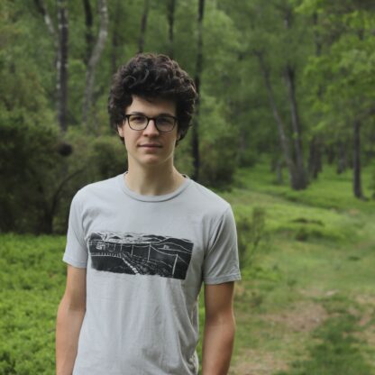 Mann in grüner Landschaft mit handbedrucktem T-Shirt mit einem Linolschnitt, der eine schwedische Schären Landschaft zeigt