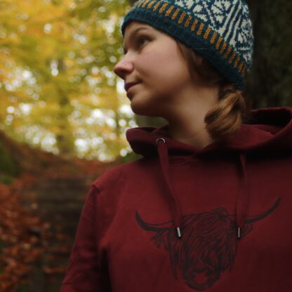 Handbedruckter Hoodie mit einem Highland Rind als Motiv, Frau mit Strickmütze im herbstlichen Wald