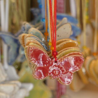 Keramikanhänger Schmetterling mit Stempeldruck in verschiedenen Farben, auf farbigem Band mit Perle aufgefädelt.